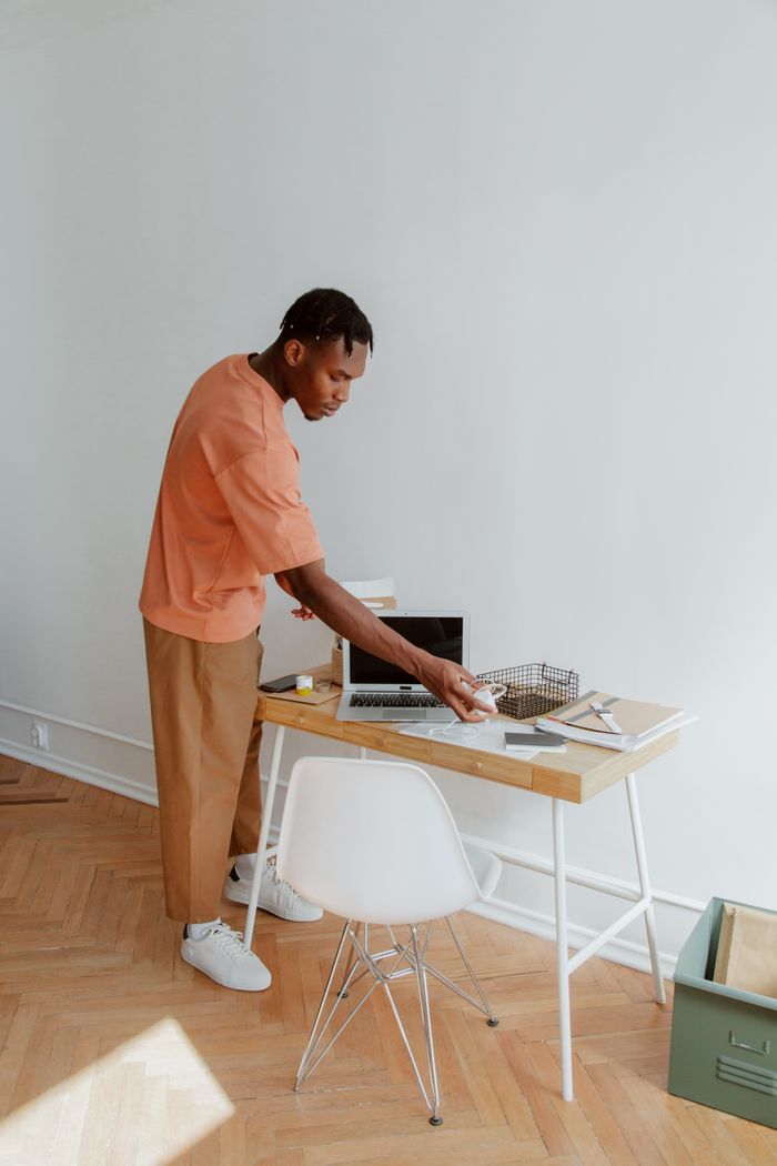 A man standing at a desk organizing papers and electronic devices in a modern office setting.